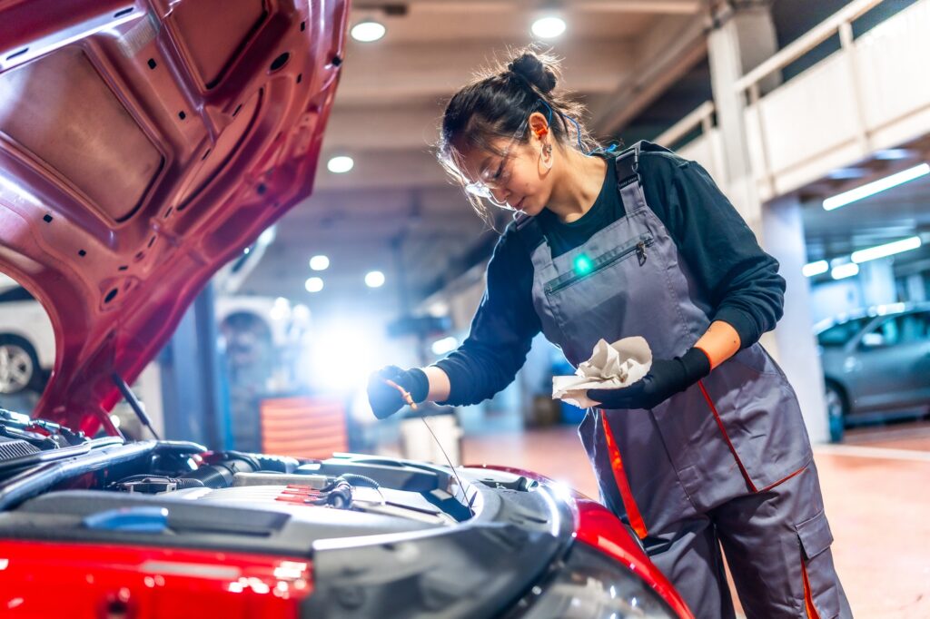 Female mechanic checking oil level in car engine at garage